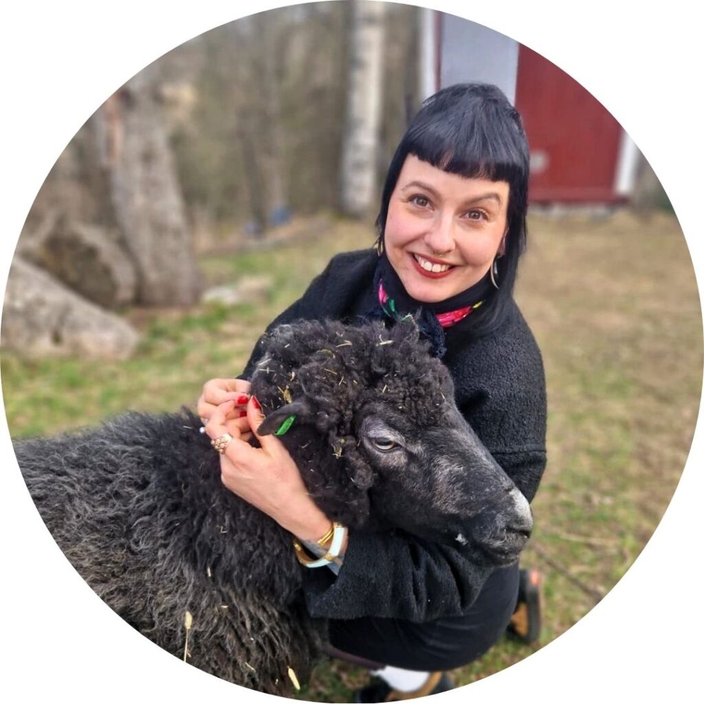 tummahiuksinen nainen halaa ulkona mustaa lammasta ja katsoo kameran suuntaan